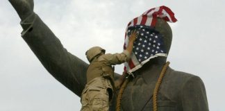 Un infante de marina estadounidense cubre el rostro de la estatua de Saddam Hussein en Bagdad días después de la invasión. La estatua luego fue derribada, convirtiéndose en una símbolo del derrocamiento del líder iraquí. GETTY