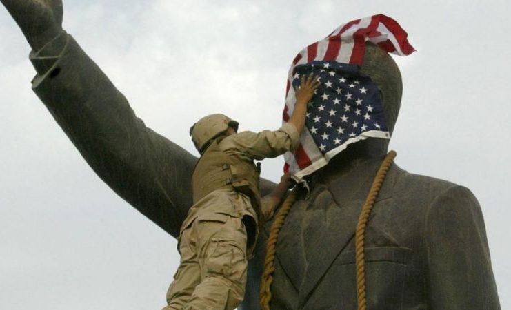 Un infante de marina estadounidense cubre el rostro de la estatua de Saddam Hussein en Bagdad días después de la invasión. La estatua luego fue derribada, convirtiéndose en una símbolo del derrocamiento del líder iraquí. GETTY